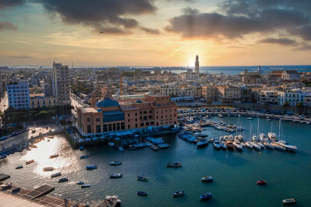 Quali sono le zone più pericolose di Bari? 2 Teatro Margherita al tramonto, storica sala teatrale su palafitte nel porto di Bari con vista panoramica su Bari Vecchia e mare Adriatico. Iconico edificio culturale che si specchia nelle acque del porto tra barche da pesca e yacht nel cuore della città pugliese. Simbolo dell'architettura liberty di Bari Puglia e tappa imperdibile per turismo culturale e fotografia paesaggistica al crepuscolo.